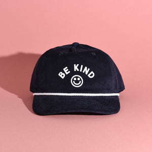 Navy blue corduroy cap with 'BE KIND' text and smiley face on a pink background
